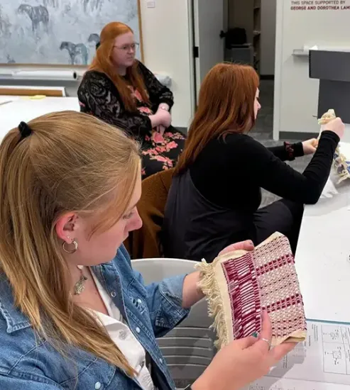 A group of students, with one student focused on a vibrant woven piece in her hands.