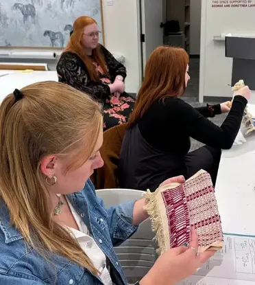 A group of students, with one student focused on a vibrant woven piece in her hands.