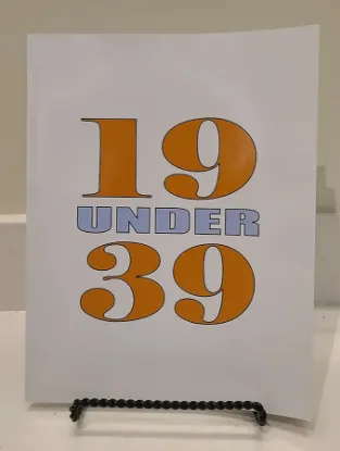 the 19 under 39 book resting on a book stand, the cover features the number 19 and 39 large and stacked vertically with the text under between them