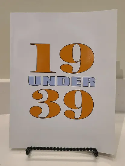 the 19 under 39 book resting on a book stand, the cover features the number 19 and 39 large and stacked vertically with the text under between them