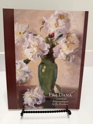 Fra Dana book resting on a bookstand with the text American Impressionist in the Rockies and a impressionist painting of a vase of white flowers on the cover