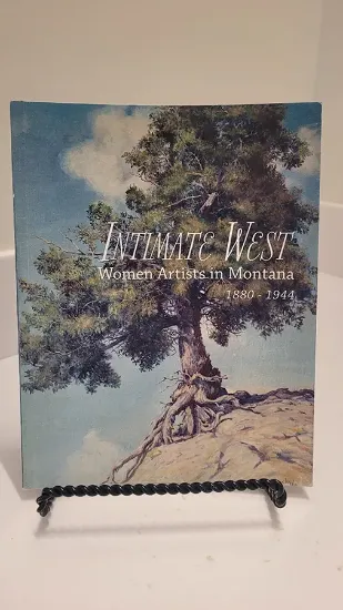 intimate west book resting on a bookstand with text women artist in montana 1880-1944 below the title and a painting of a lone tree on a cliffside in the background