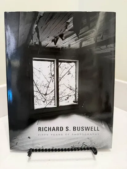 Fifty years of photography cover featuring black and white image of a room with a broken window with snow piled on the floor and paint peeling from the ceiling.