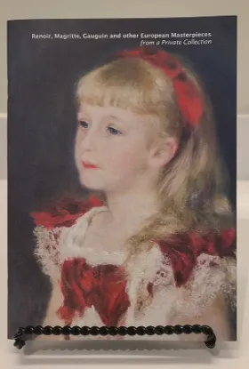 Renoir, Magritte, Gauguin book resting on a bookstand with a painting of a little girl in a white dress with red ribbon highlights