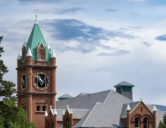 view of clocktower and roof of University Hall with blue sky laced with white clouds in the background