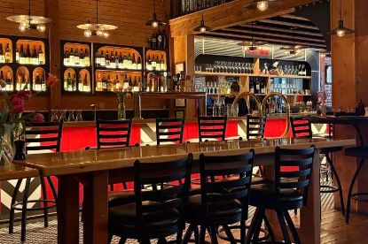 Warmly lit bar of the Brasserie Porte Rouge with a long high-top table and black chairs, red bar front, and shelves of backlit liquor bottles and glassware.