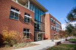 Brick and glass College of Education building with large windows and a central glass entryway along a sidewalk under a clear blue sky.